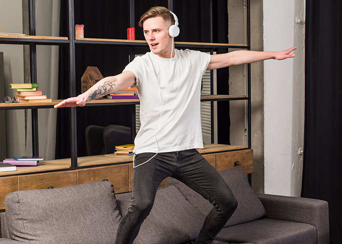 Young man wearing headphones and balancing on a couch, illustrating the concept of the most pathetic injuries shared by people.