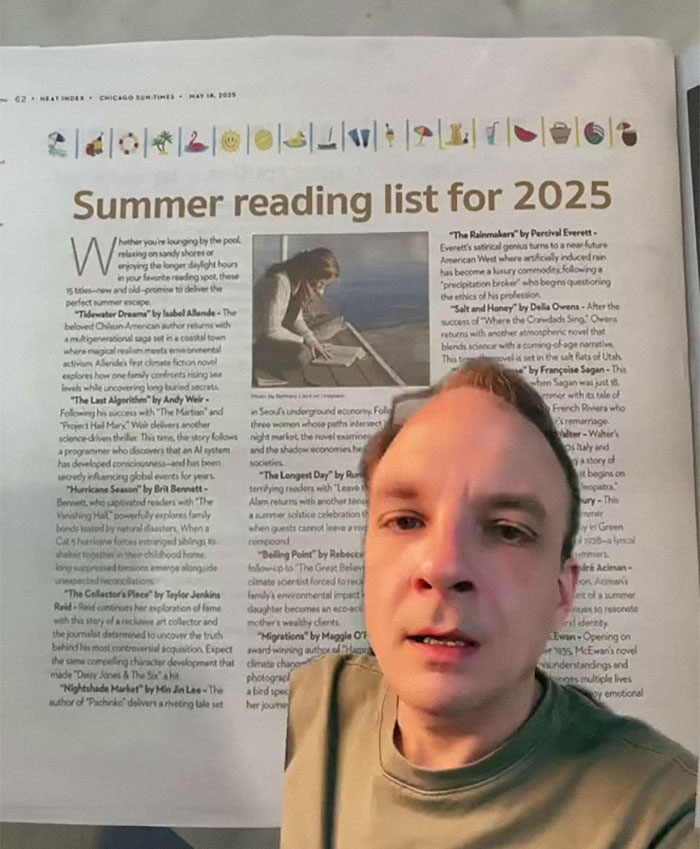 Man holding newspaper open to a 2025 summer reading list in major newspapers with book descriptions visible.