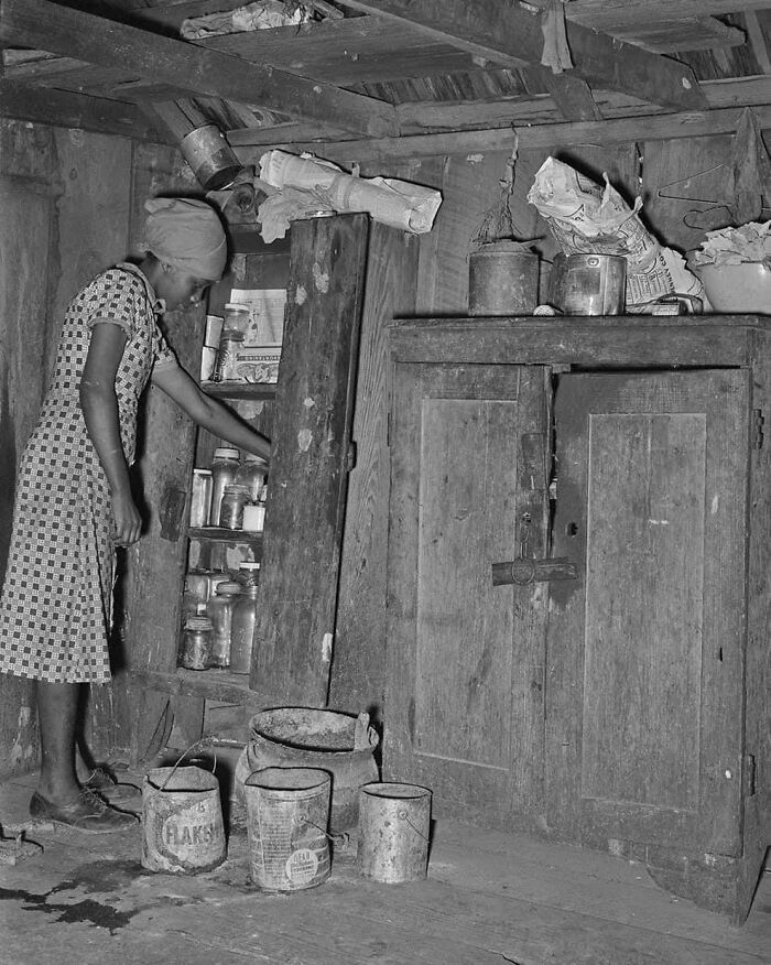 Black and white photo of a woman organizing jars in a rustic kitchen, a side of history rarely shown in textbooks