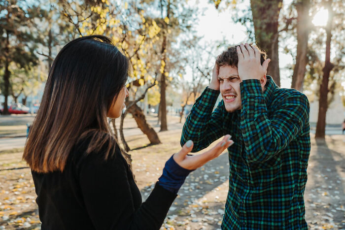A stressed man holding his head during an intense argument with a woman in a park, depicting life blunders tension.