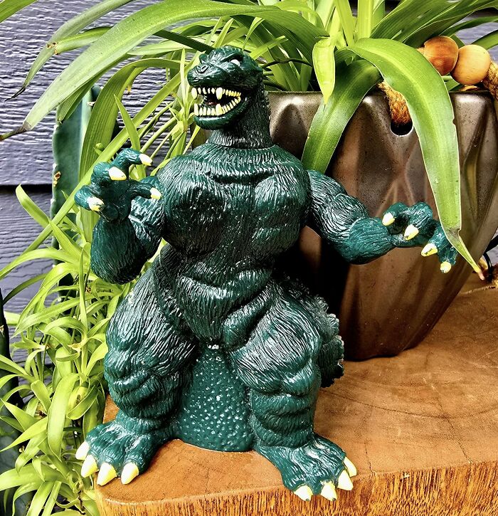Green vintage Godzilla toy with exaggerated muscles displayed among potted plants as a thrifted weird and wonderful find.