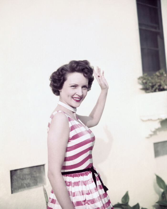 Smiling woman in vintage striped dress waving, a rare historical photo showing the side of history not in textbooks.