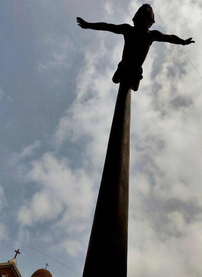 Silhouette of a child balancing on tall pole against cloudy sky, captured in pure street photography style.