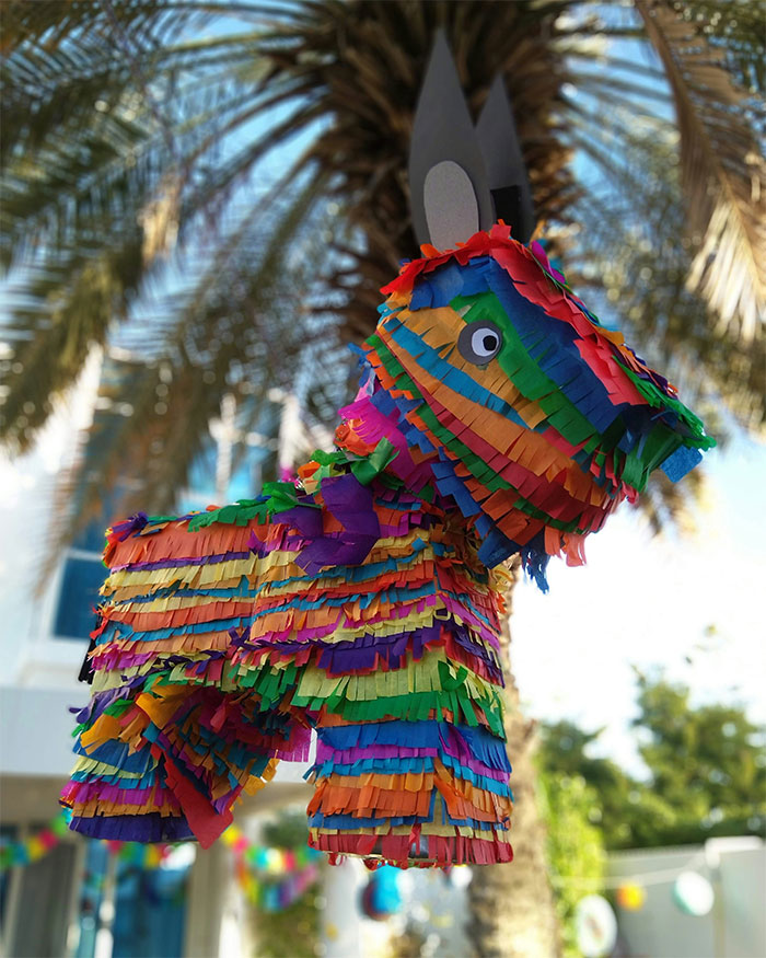 Colorful pi&ntilde;ata hanging outdoors with palm trees in background, related to mom stealing pregnancy announcement and gender reveal.