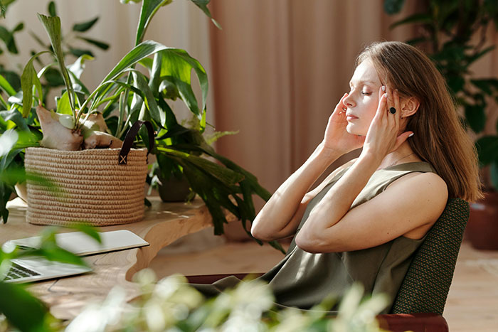 Woman sitting at desk surrounded by plants, appearing stressed, reflecting on couple and bully bro wedding conflict.