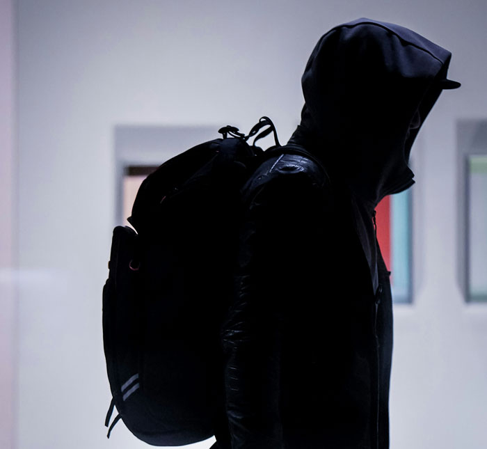 Person wearing a hooded jacket and backpack in shadow, representing unsuccessful mugging attempts by strangers.