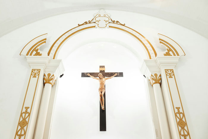 Crucifix on a church wall with ornate gold and white archway, symbolizing faith related to cults and escapes.