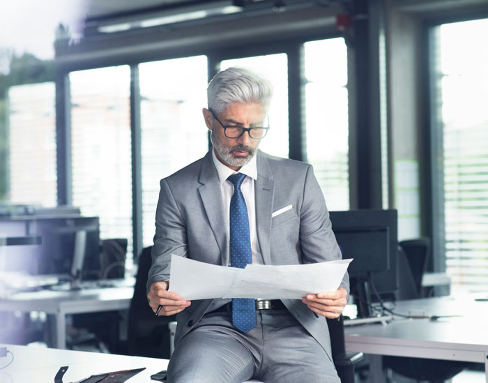 Mature businessman in a gray suit reading documents in a modern office, representing bosses going off the rails.
