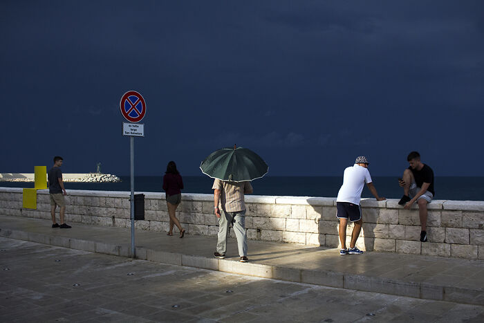People enjoying a moody evening by the sea, highlighting street photography moments with dramatic lighting and shadows.