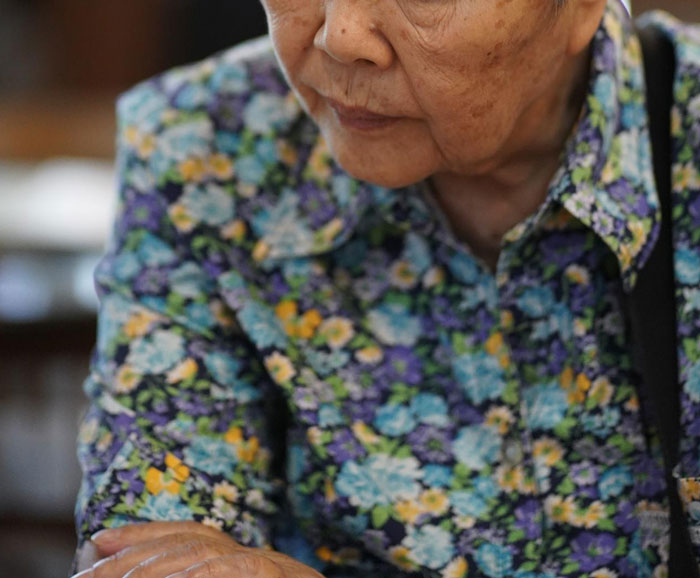Elderly woman in a colorful floral shirt looking down, reflecting on family conflict and caring for his mom issues online. Elderly woman in a colorful floral shirt looking down, reflecting on family conflict and caring for his mom issues online.