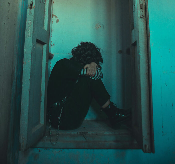 Person sitting alone in a dim, blue-toned room, hugging knees, reflecting on lost friendship of over 10 years.