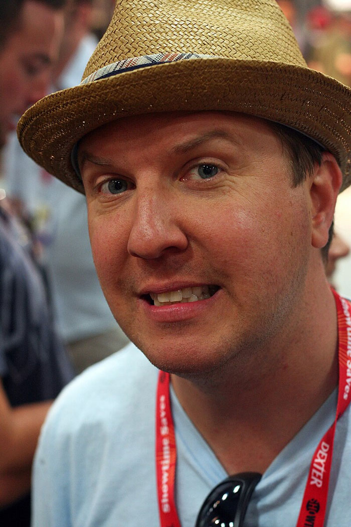 Close-up of a man wearing a straw hat and a red lanyard at a celebrity encounters event.