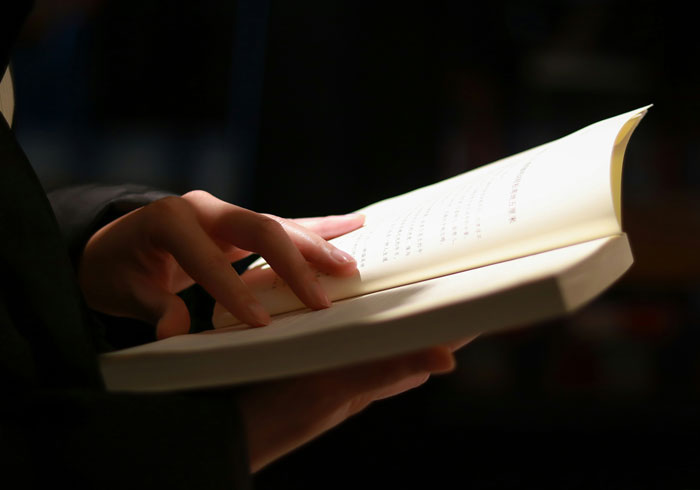 Person holding and reading a book under warm light illustrating 2025 summer reading list runs in newspapers.