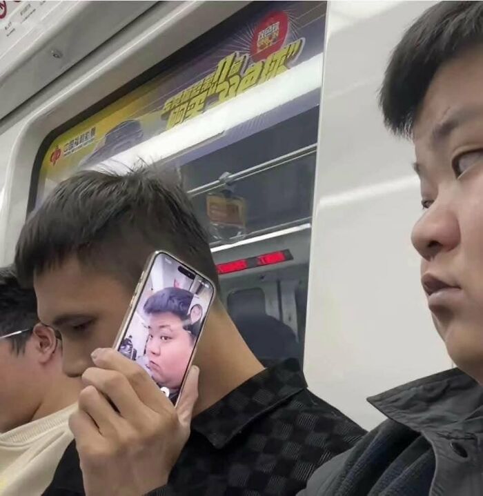 Man on subway holding phone showing a chaotic meme of another man's face, capturing chaotic memes for boredom relief.