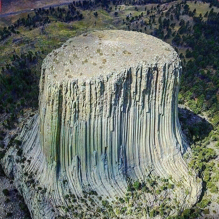 Aerial view of Devils Tower rock formation surrounded by trees, showing a hidden side of history not in textbooks.