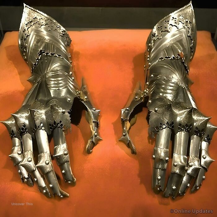 Pair of intricately designed medieval gauntlets displayed on an orange cloth, highlighting ancient history armor craftsmanship.