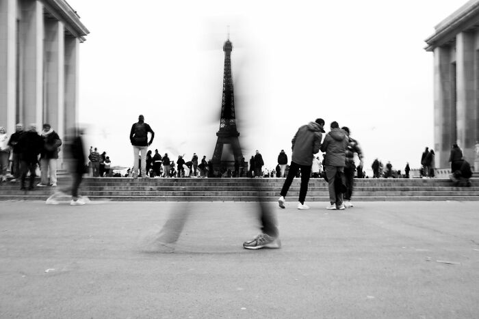 Black and white street photography capturing blurred pedestrians with the Eiffel Tower in the background, showcasing street photography art.