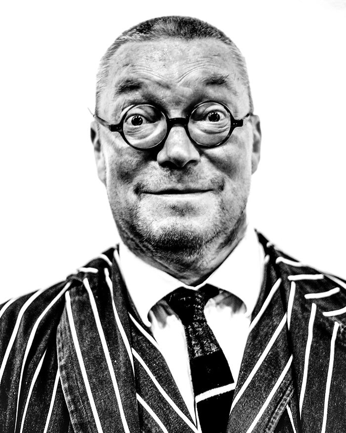 Close-up black and white portrait of a man with round glasses wearing a striped suit, capturing creative world food photography awards style.