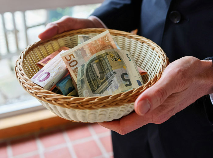 Hands holding a basket filled with euro banknotes, illustrating the financial aspects some people faced after escaping from cults.