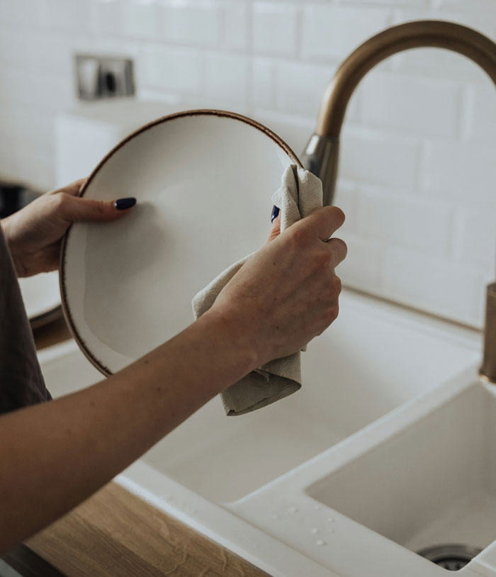 Person drying a plate by the kitchen sink with a towel, illustrating infuriating things said by people in charge concept.