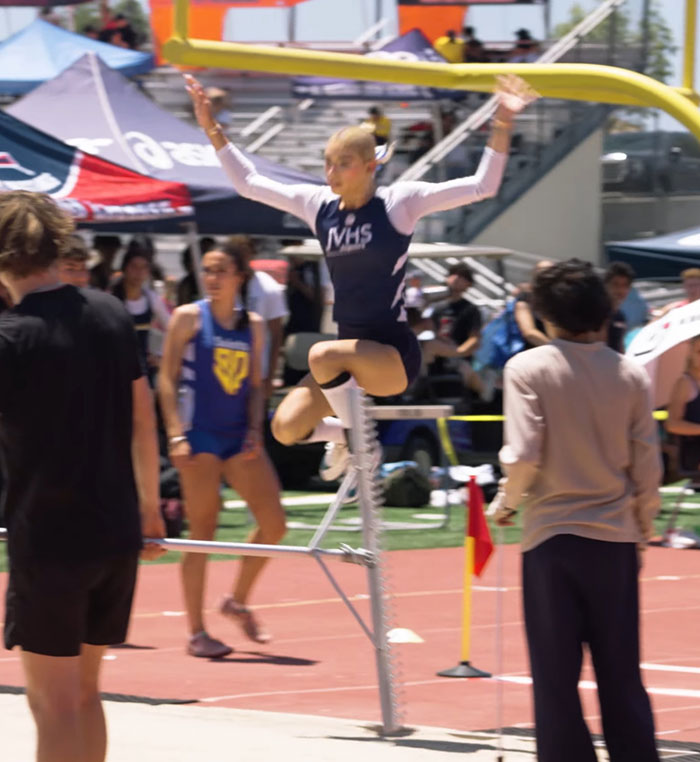 High school girl athlete jumping during a track and field event, showing defiant spirit on the competition podium.