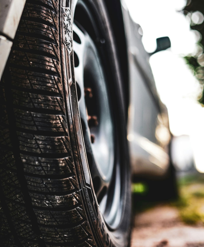 Close-up of a dirty car tire showing wear, illustrating ways people lose money while thinking they’re saving on vehicle maintenance.