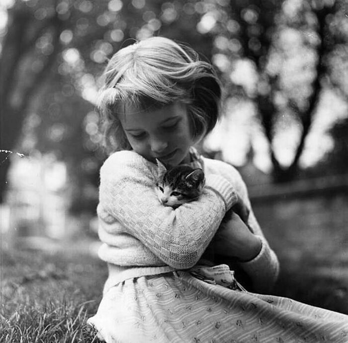 Young girl gently hugging a cat in a vintage black and white photo, showcasing the timeless bond between kids and cats.