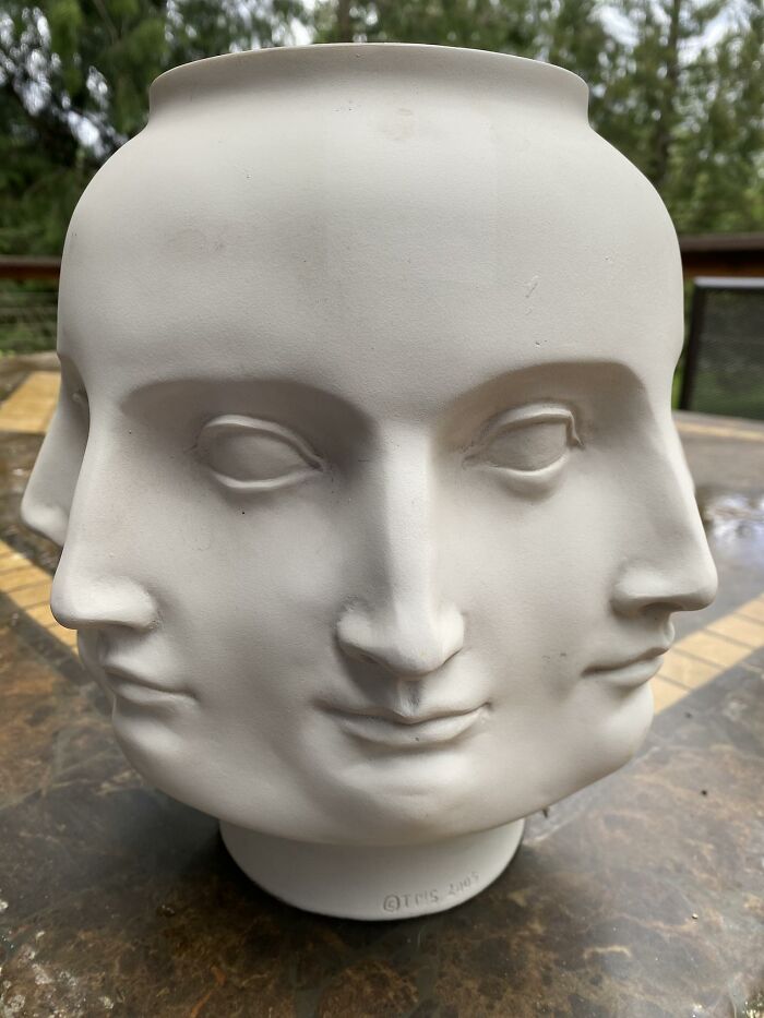 Thrifted ceramic vase with three sculpted faces, a weird and wonderful collectible display item outdoors.