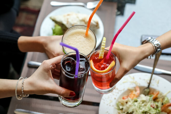 Three people clinking glasses of drinks at a table with food, illustrating everyday items becoming stupid expensive.