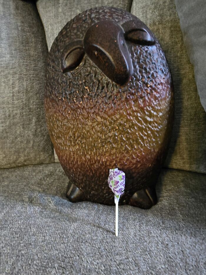Large textured bird sculpture on a gray couch next to a grape-flavored lollipop, a weird and wonderful thrifted find.