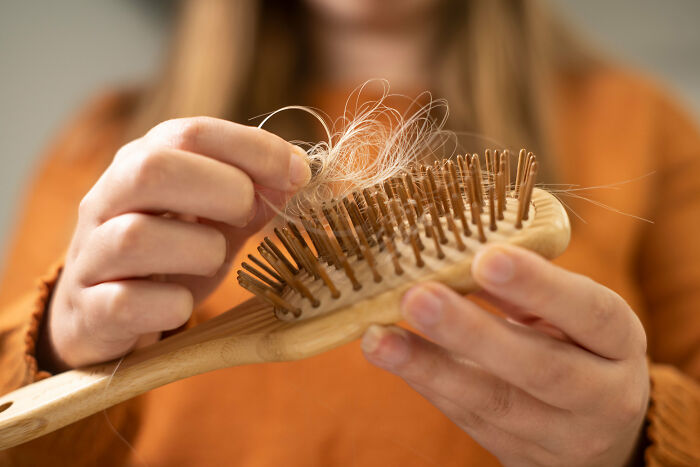 Person holding a wooden hairbrush with tangled hair, illustrating cultural differences in personal grooming habits.