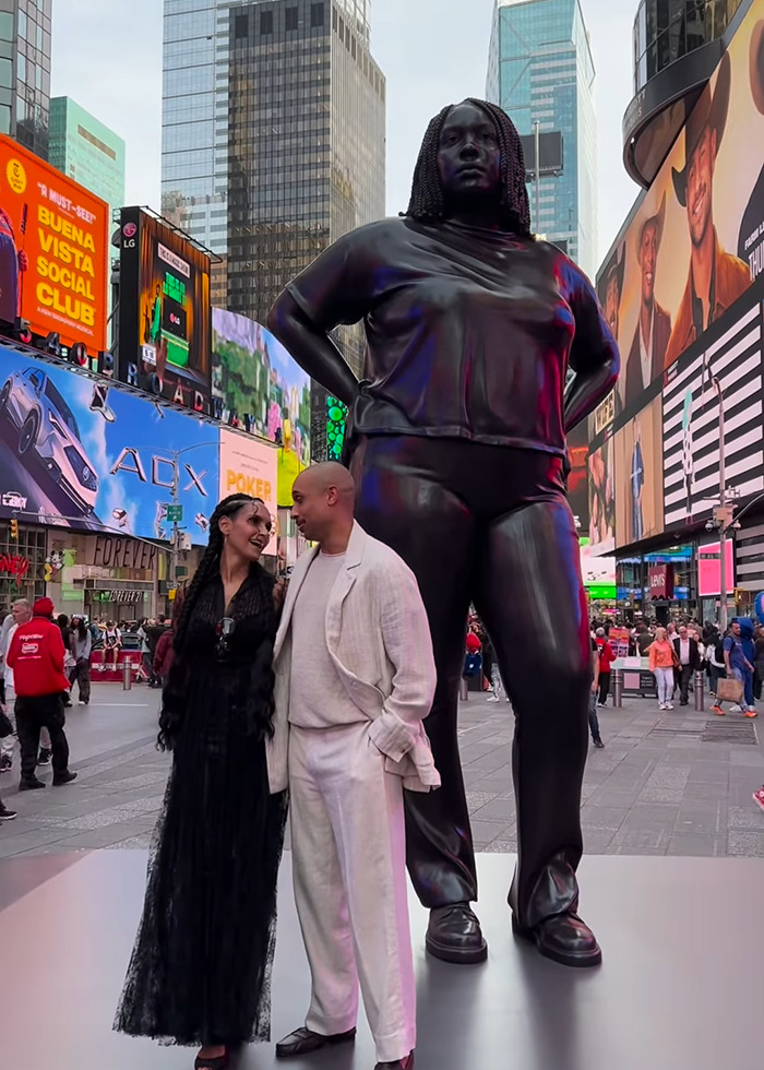 Statue of Black woman in NYC Times Square with people nearby amid urban billboards and crowds.