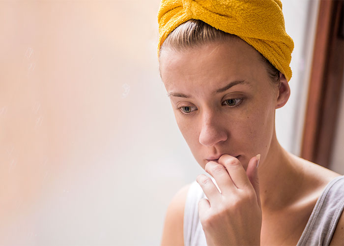 Young woman with a yellow towel on her head looking thoughtful and anxious, reflecting on things everyone does but doesn't talk about.