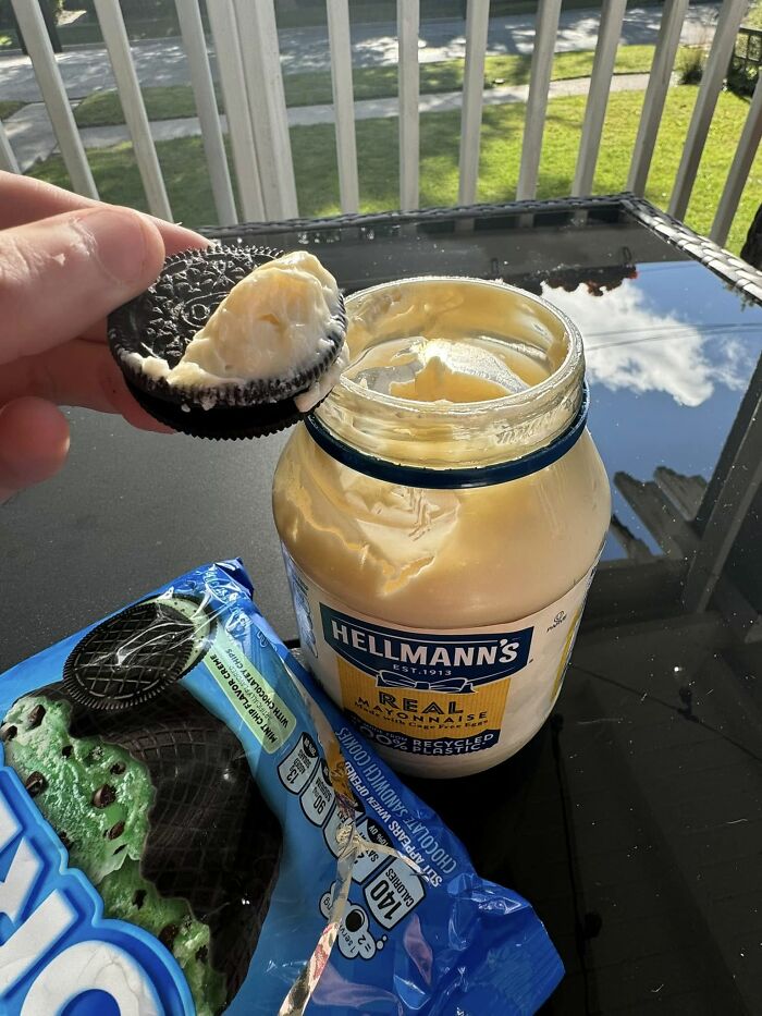 Oreo cookie with mayonnaise filling being held above an open jar of mayonnaise on a glass table outside cursed food pics.