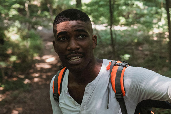Young man in a forest wearing a backpack, expressing a scared gut feeling to leave now during a hike.