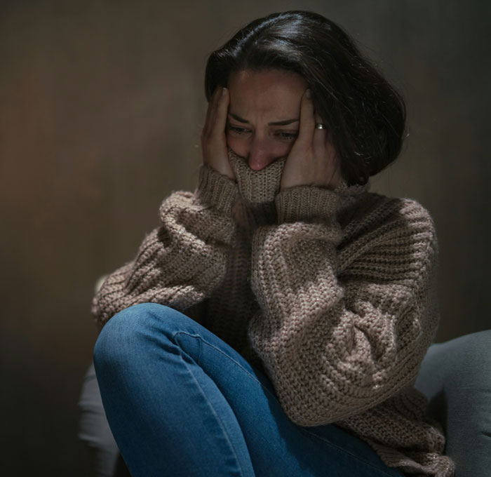 Woman in a cozy sweater sitting with knees up, holding her head in distress over friendship of 10 plus years ended.
