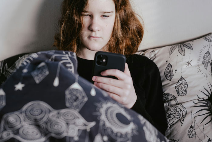Teen girl in bed focused on smartphone, reflecting on weird rules parents had during childhood and growing up experience.