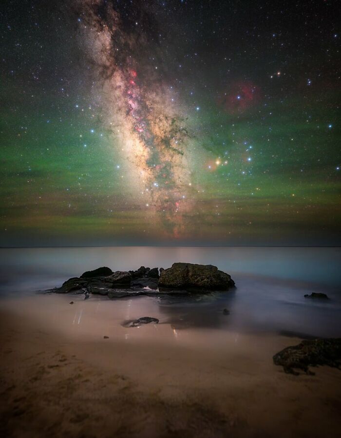 Milky Way shining brightly over a calm rocky beach under a clear night sky filled with stars.