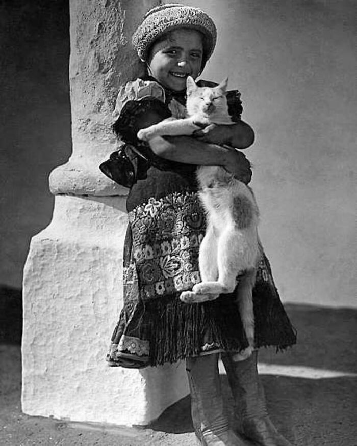 Vintage photo of a smiling child holding a relaxed cat, showcasing the timeless bond between kids and cats.