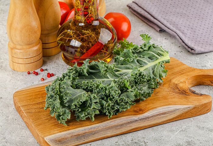 Fresh kale on a wooden cutting board with tomatoes, olive oil, and wooden pepper grinders for wild cooking opinions.