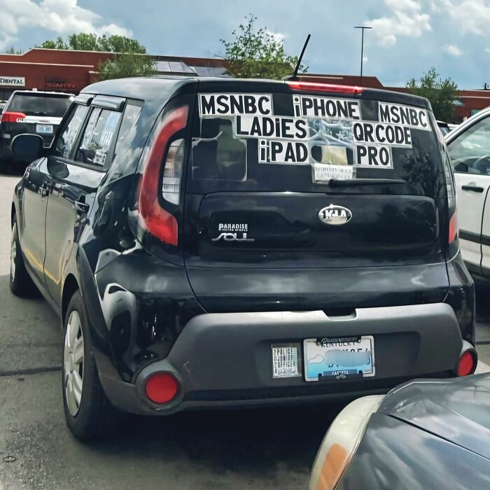Black Kia Soul parked in a lot with outrageous hot takes stickers displayed on the rear window and bumper area.