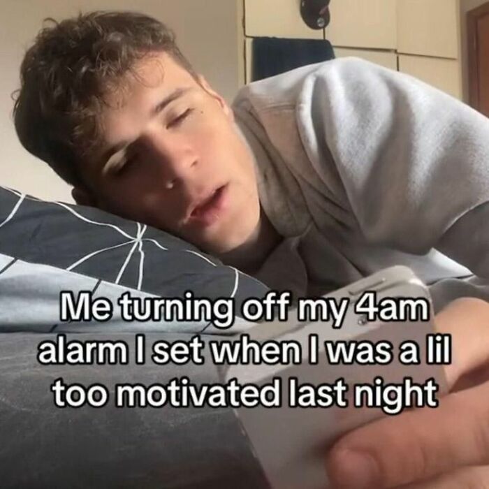 Young man in a hoodie lying in bed, looking tired while turning off a 4am alarm, funny random memes humor concept.