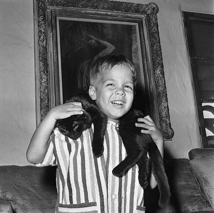 Vintage photo of a happy boy holding a black cat on his shoulders, showcasing the timeless bond between kids and cats.