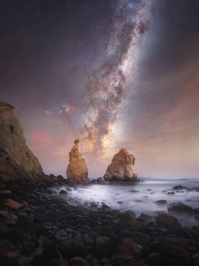 Milky Way shining brightly over rocky coastline with smooth ocean waters under a star-filled night sky.
