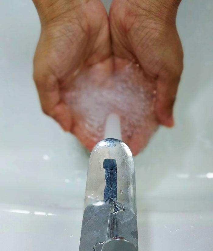 Hands cupped under a running faucet showing a habit related to being raised poor and water conservation.