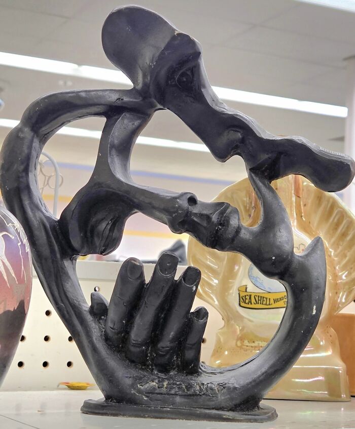 Abstract black sculpture of intertwined faces and hands, a strange thrifted find with weird and wonderful design elements.