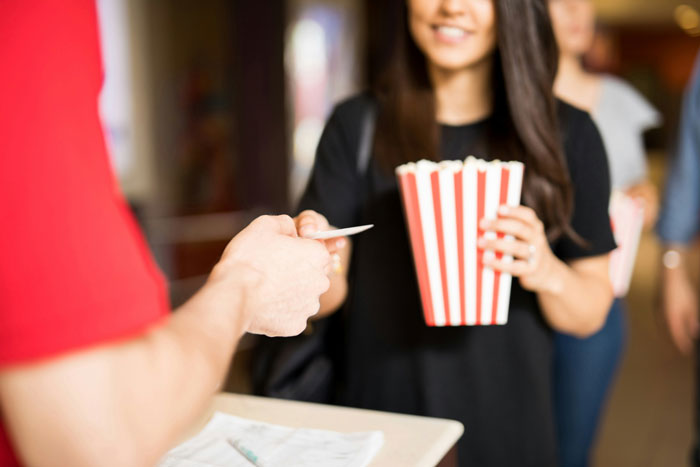 Person handing ticket to smiling woman holding popcorn, representing former employees revealing disturbing workplace secrets.
