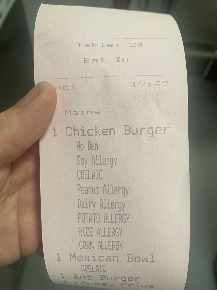 Hand holding a hospitality order receipt listing multiple allergy notes for a chicken burger and Mexican bowl.