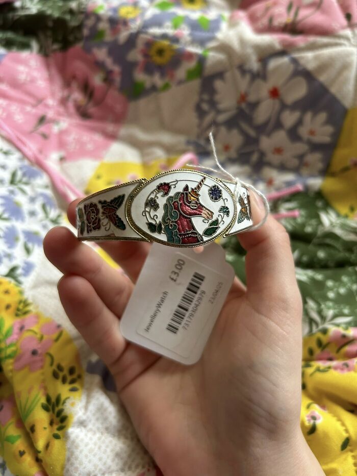 Hand holding a thrifted unicorn bracelet with detailed designs, showcasing weird and wonderful vintage finds.