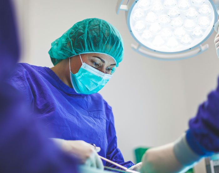 Experta en autopsias con mascarilla y gorro quirúrgico realizando una intervención bajo luces de quirófano.